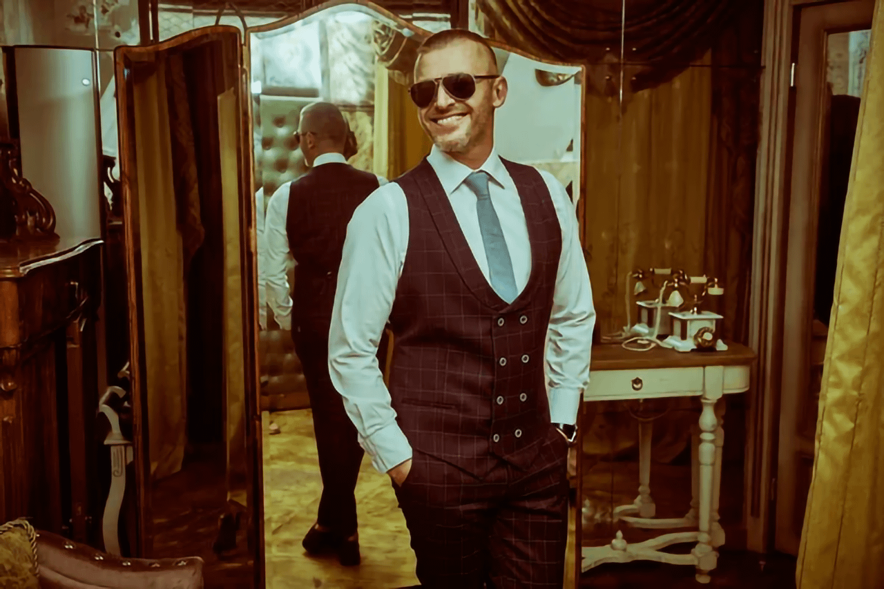 Uomo sorridente in abito elegante davanti a uno specchio, esempio di dandy moderno.