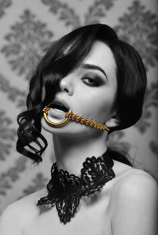 Ritratto in bianco e nero con accessorio dorato e collarino in pizzo che interpreta il fetish di lusso con eleganza
