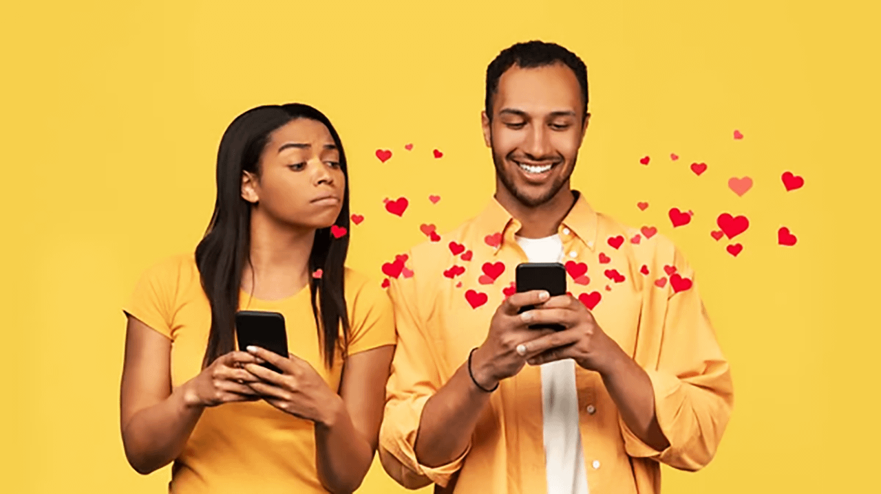 Donna gelosa osserva il partner che sorride guardando il telefono, simbolo di insicurezze nel rapporto di coppia.