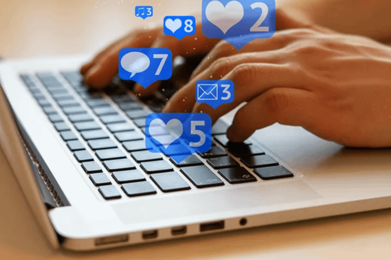 Mani su una tastiera con icone di cuori, commenti e messaggi che simboleggiano i contenuti raw nei social media - Pommenor