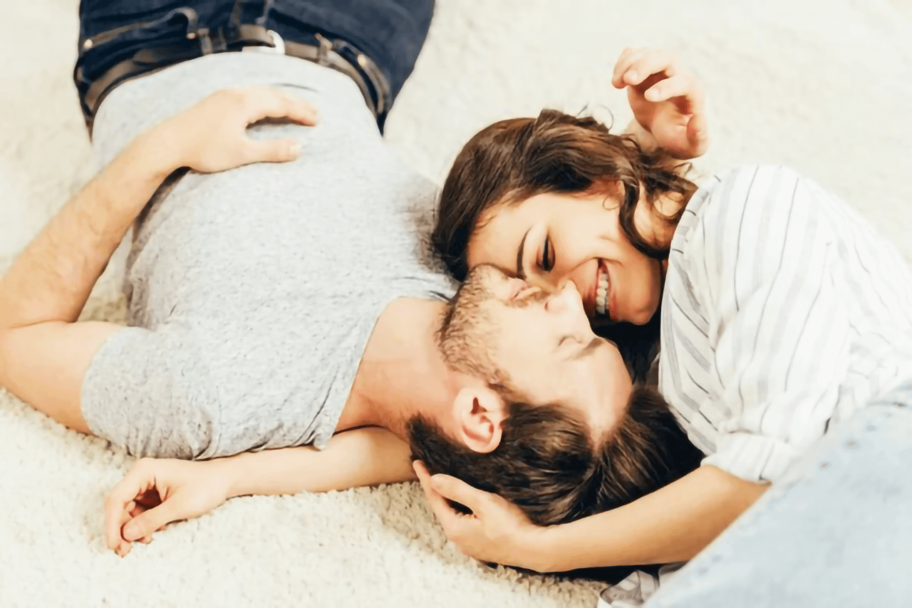 Coppia giovane distesa su un tappeto che si abbraccia e ride durante un momento romantico e intimo