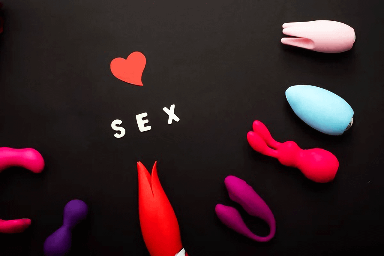 Collezione di sex toys colorati e scritta SEX con cuore su sfondo nero