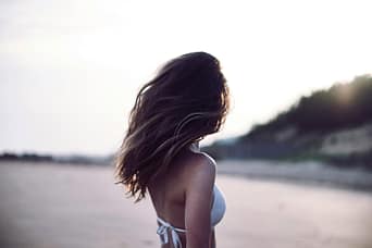 Donna sensuale sulla spiaggia con i capelli mossi, simbolo del gesto erotico di tirare i capelli – Pommenor