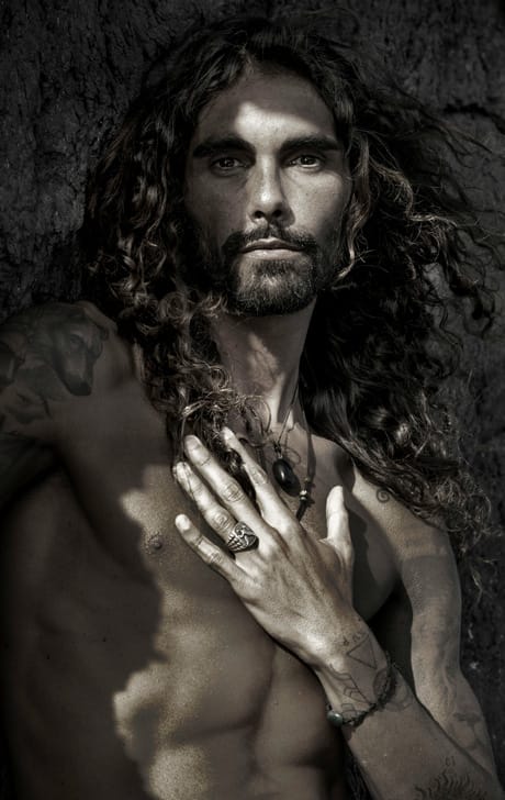 Uomo affascinante con capelli lunghi e tatuaggi, rappresentazione dell’energia sensuale nella mindfulness sessuale con Pommenor.