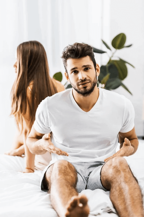 Uomo e donna seduti sul letto che affrontano difficoltà a raggiungere l'orgasmo, simbolo di tensione nella coppia.