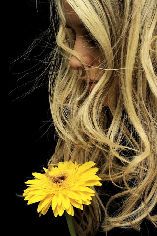 Primo piano di una donna con capelli biondi e un fiore giallo, simbolo di bellezza naturale e integratori per i capelli.