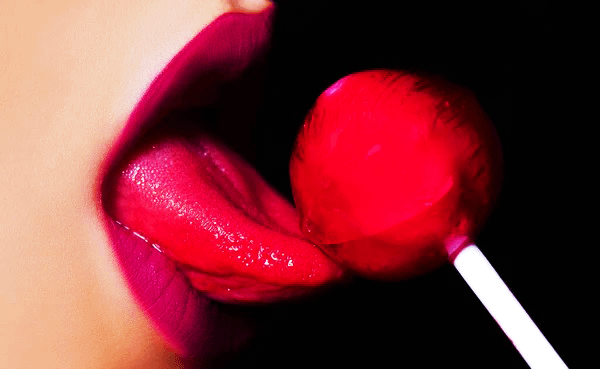 About us - Primo piano di labbra rosse lucide che leccano un lecca-lecca rosso, immagine accattivante e moderna.