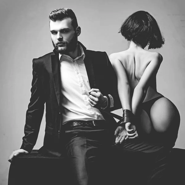 Uomo elegante in abito nero e donna in lingerie sensuale legati insieme, simbolo di consapevolezza sessuale e intimità nelle relazioni - Pommenor.