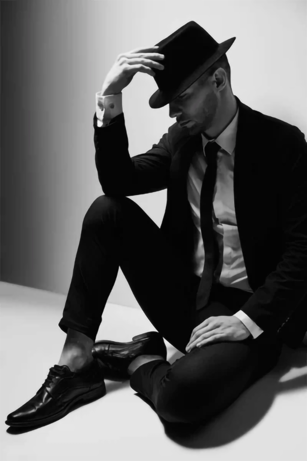 Uomo seduto con cappello e abito elegante, espressione dello stile dandy moderno.