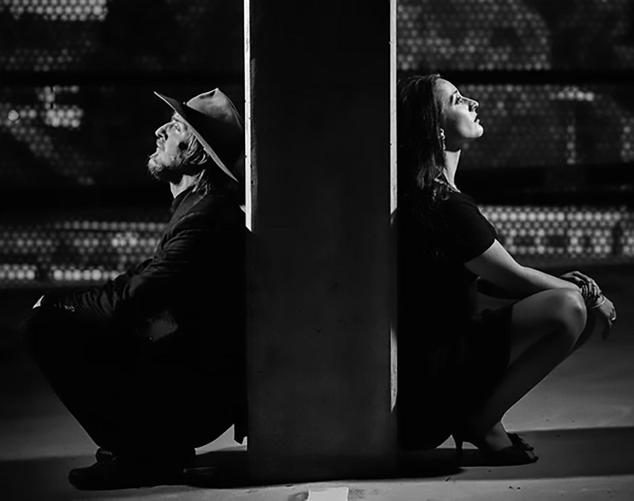 Coppia seduta schiena contro schiena, riflette sulle insicurezze nel rapporto di coppia.