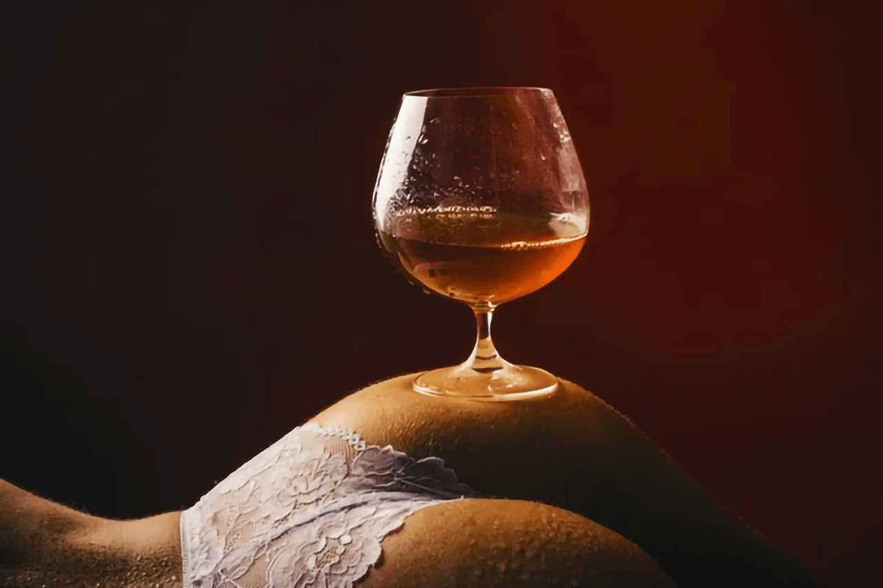 Bicchiere di cognac posato su una modella in lingerie: rappresentazione sensuale di un