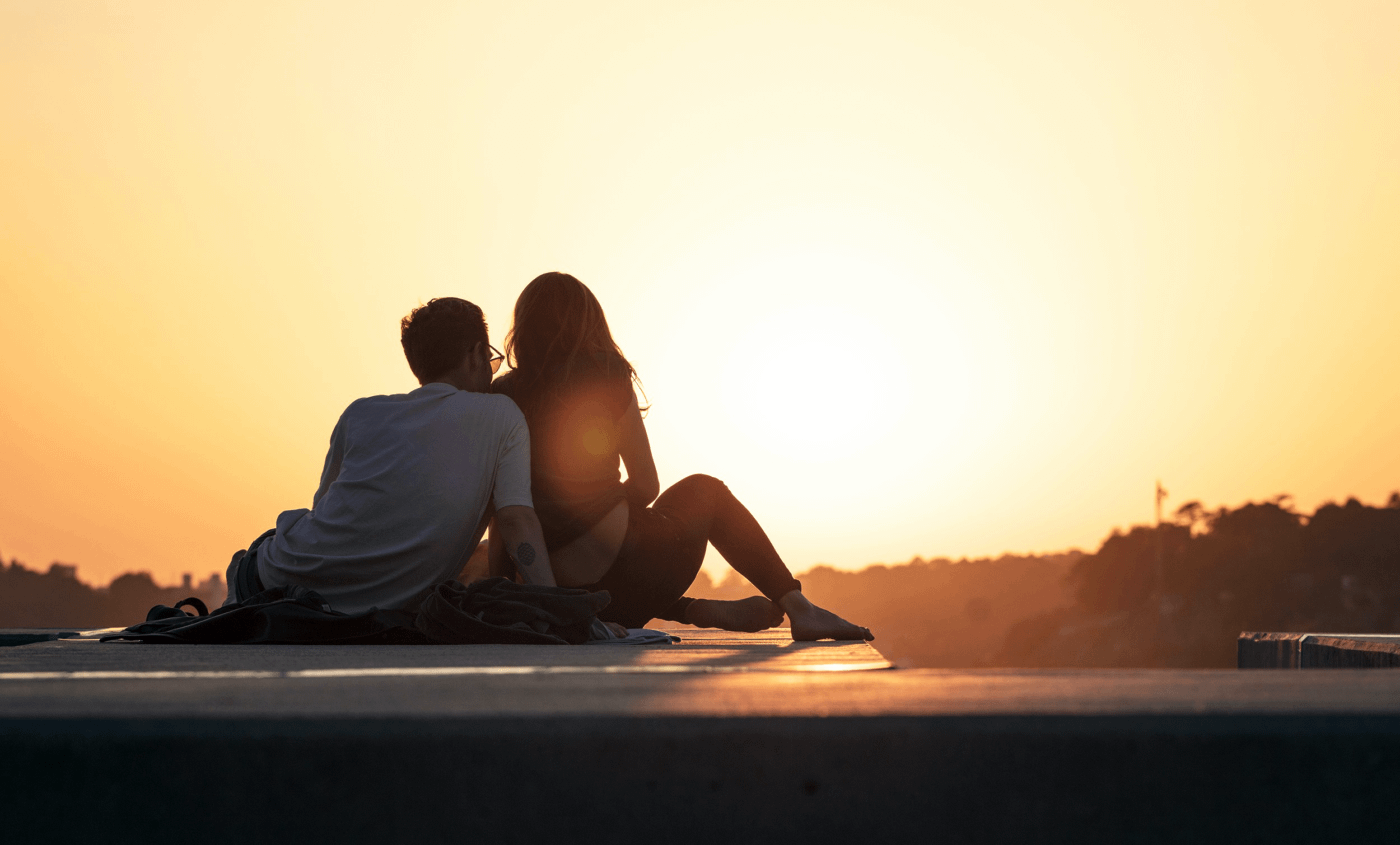 Coppia di spalle che guarda il tramonto, seduti insieme in un