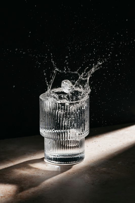 Splash d’acqua con cubetto di ghiaccio in un bicchiere trasparente – simbolo della routine ice facial Pommenor