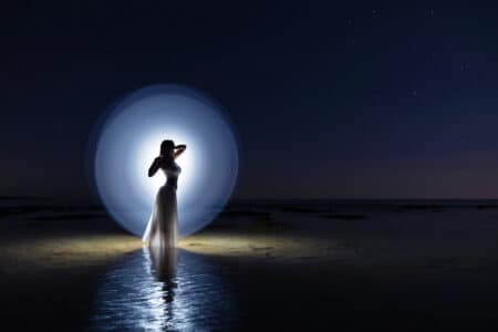 Donna elegante illuminata dal mare al chiaro di luna, simbolo del fascino e della sensualità delle escort in Puglia su Pommenor.