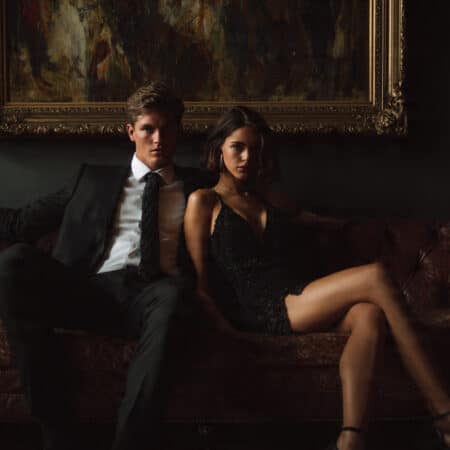 Coppia elegante seduta distante su un divano in luce soffusa, tensione emotiva percepibile