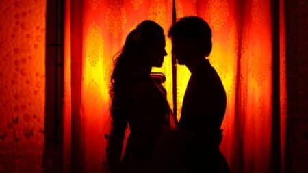 Un silhouette drammatico di una coppia abbracciata contro una tenda arancione a motivi, con retroilluminazione calda