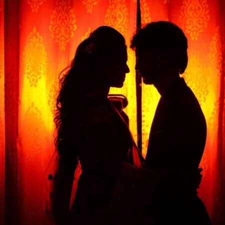 Un silhouette drammatico di una coppia abbracciata contro una tenda arancione a motivi, con retroilluminazione calda